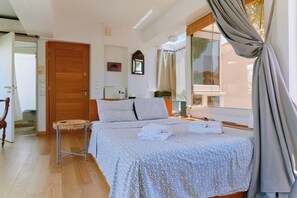 A bedroom with a bed, a wooden door, a small table, and a window with curtains.