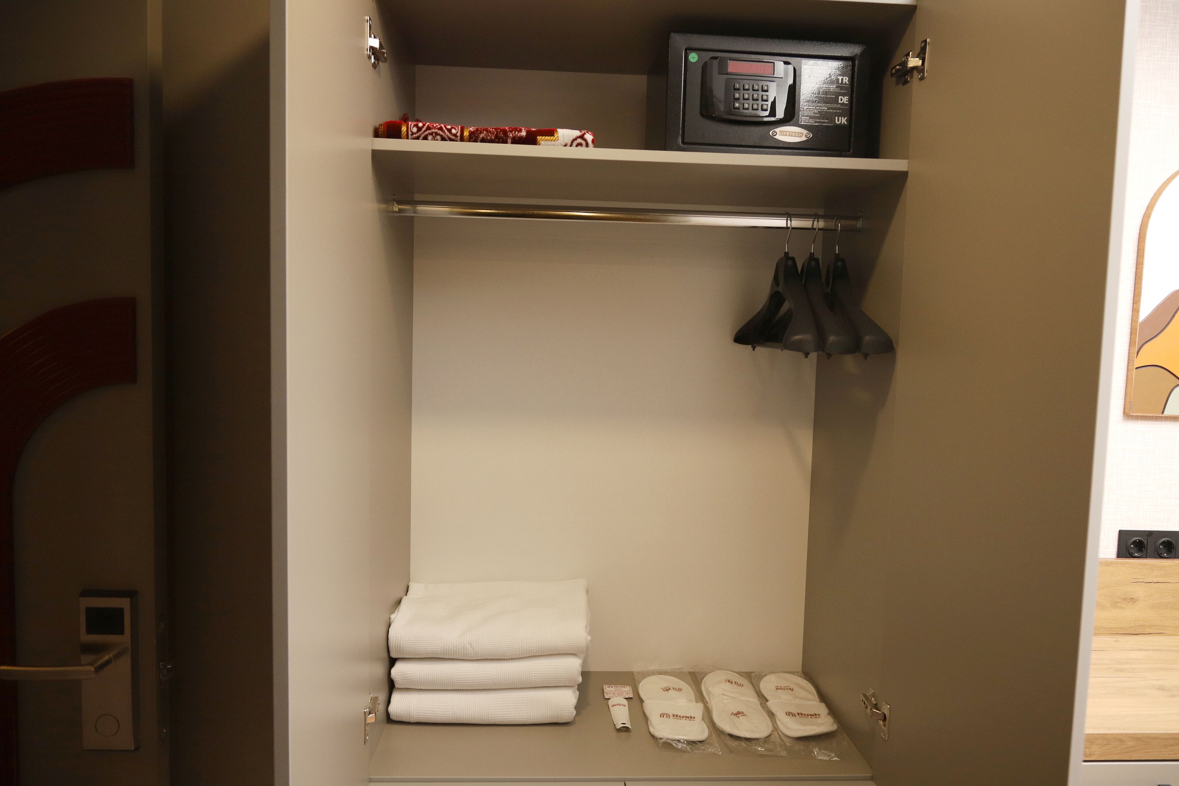 A hotel room with a minibar, a microwave, a shelf with towels, and a rack with black shoes.