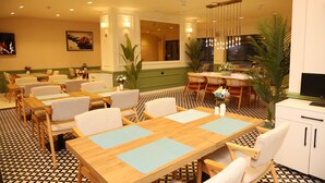 A hotel dining area with multiple tables and chairs, a television, and decorative plants. - Rush Otel Tokat (Tokat)