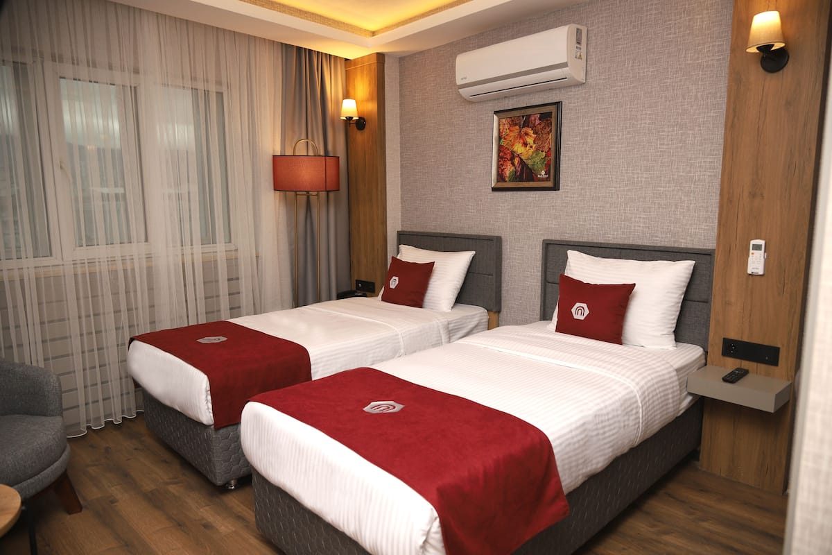 A hotel room with two beds, a desk, a chair, an air conditioner, and a painting on the wall.