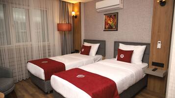A hotel room with two beds, a desk, a chair, an air conditioner, and a painting on the wall.