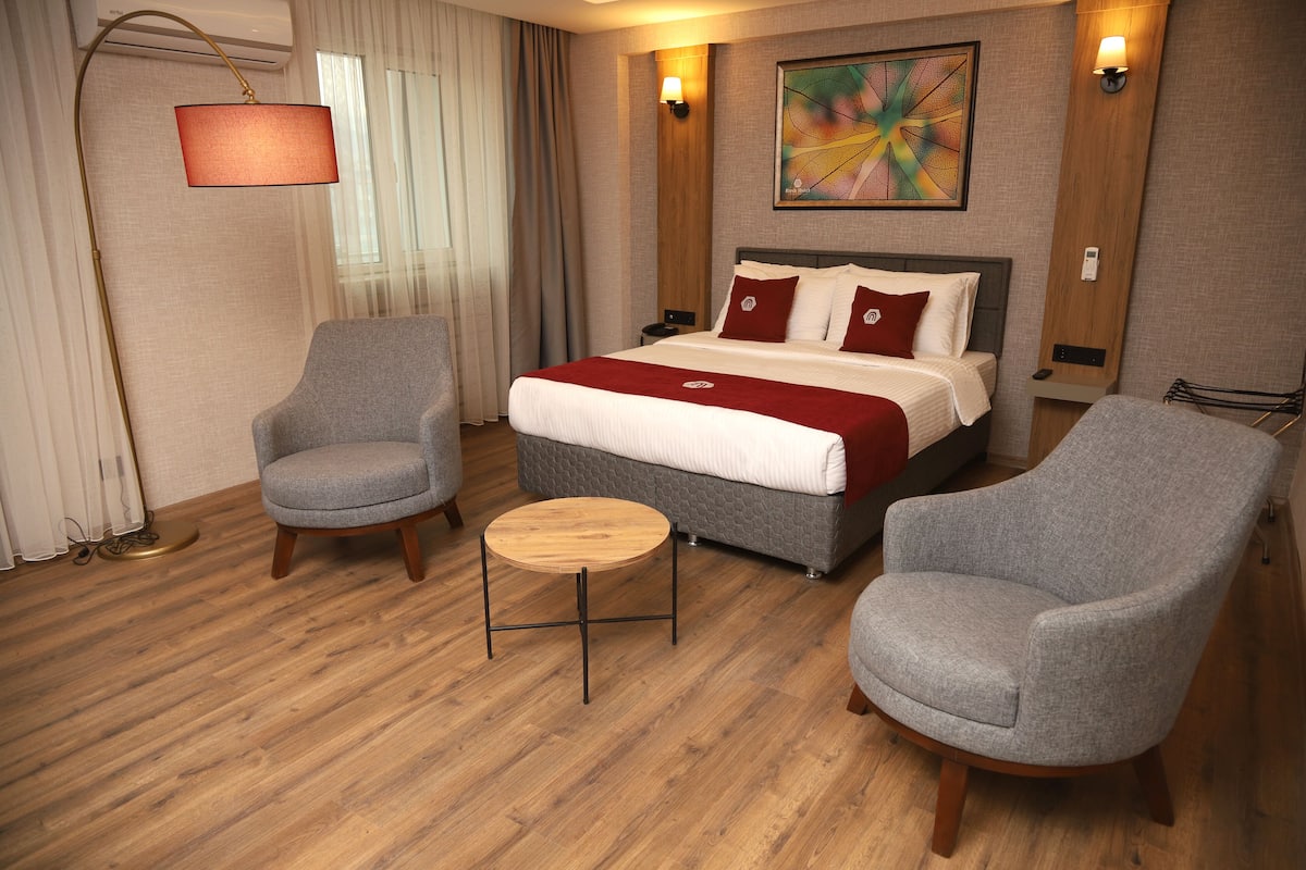 A hotel room with a bed, two armchairs, a small round table, and a floor lamp.