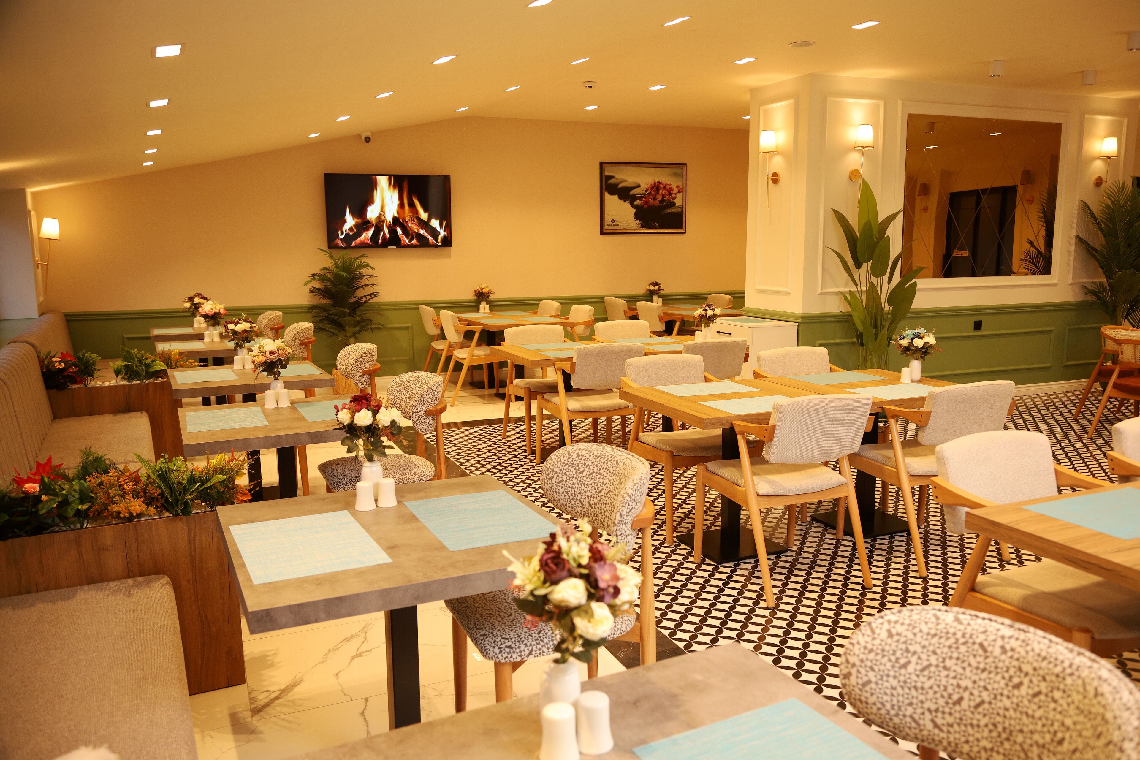 A restaurant with multiple tables and chairs, a fire display on the wall, and a large mirror.