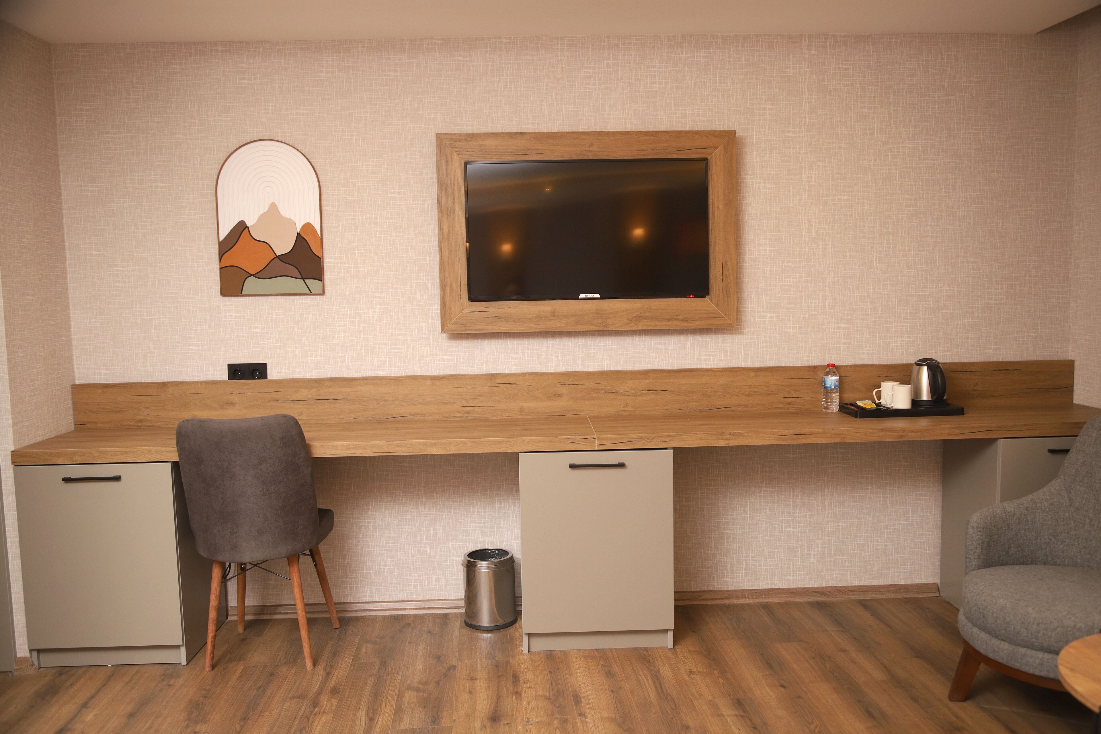 A modern room with a wooden desk, a grey chair, a small trash bin, and a wall-mounted TV.
