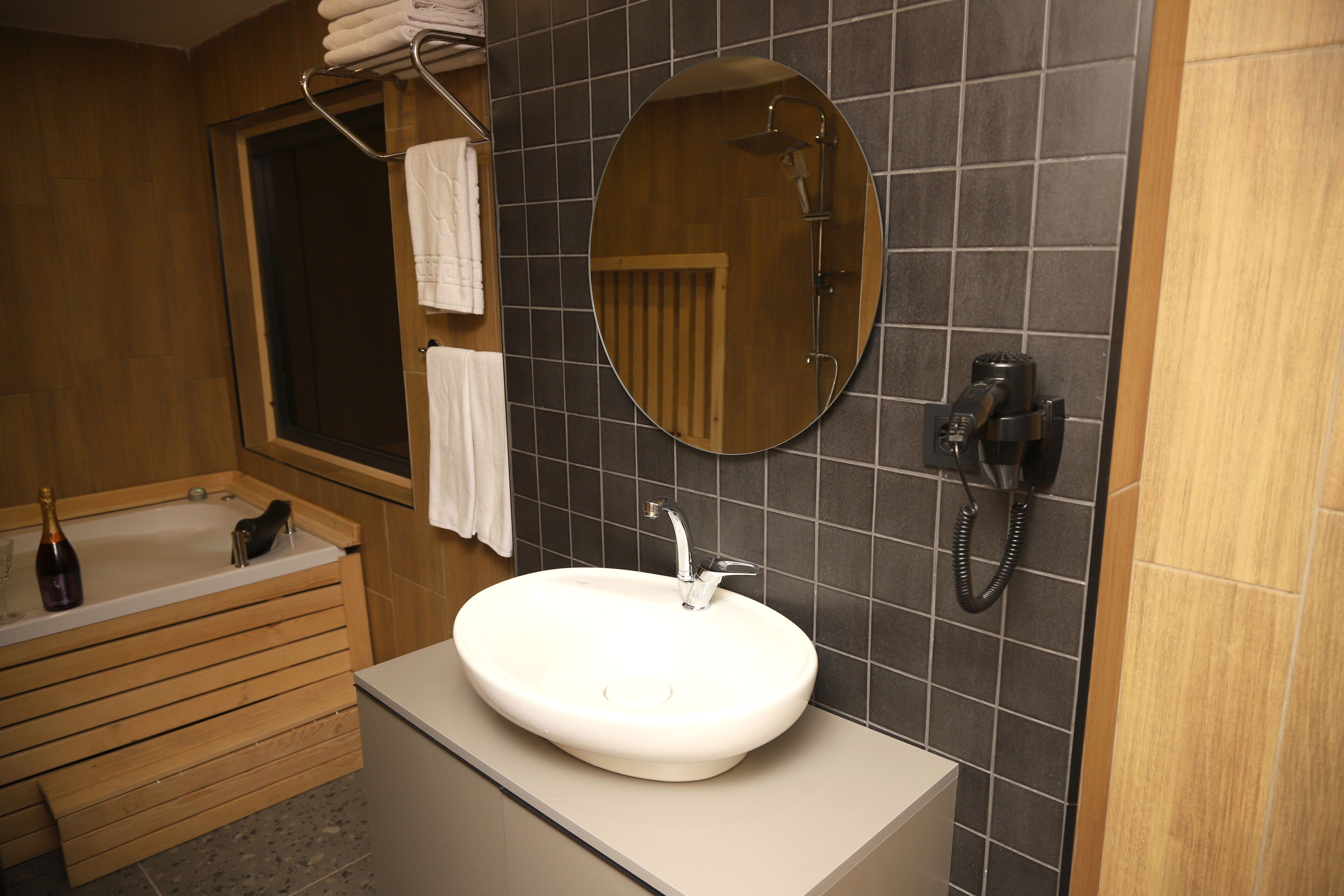 Un baño con tocador de madera, un lavamanos blanco, un espejo redondo y una zona de ducha.