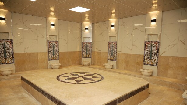 A large, well-lit bathroom with a central circular design on the floor, surrounded by four toilets and decorative wall panels. - Rush Otel Tokat (Tokat)