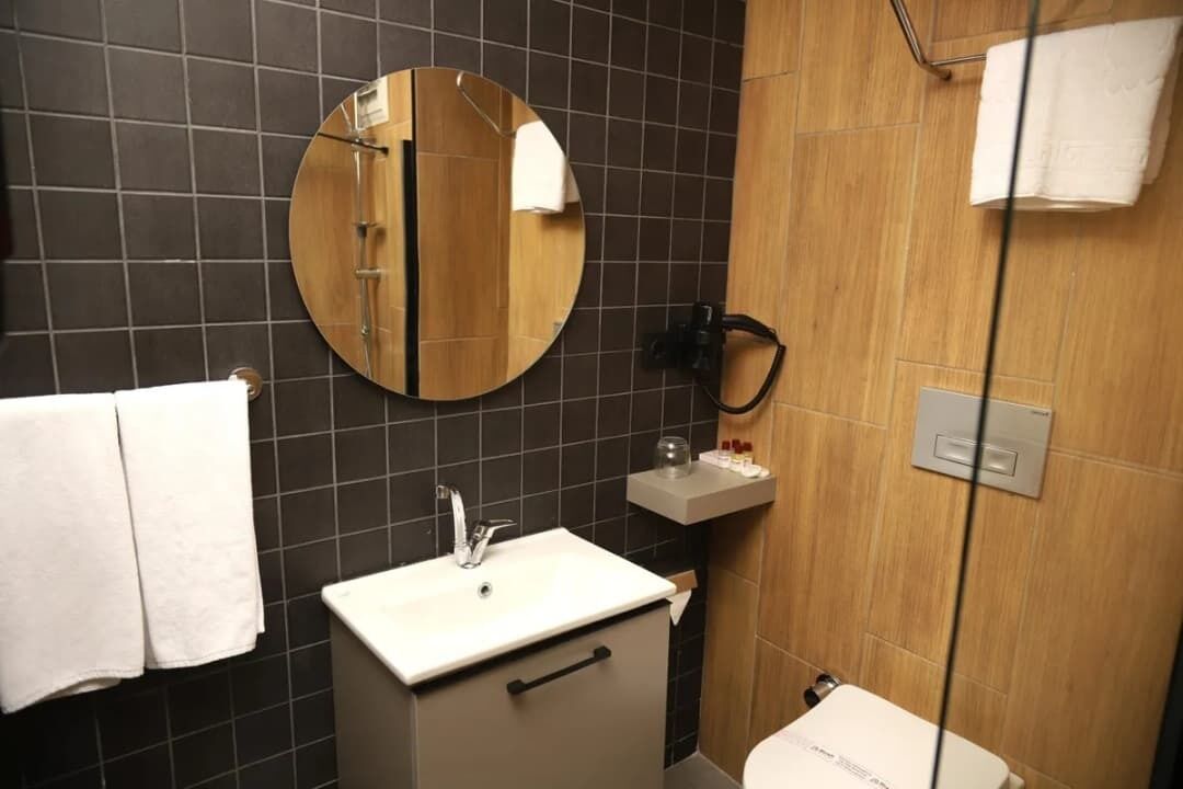Een moderne badkamer met een ronde spiegel, een witte wastafel en een toilet.