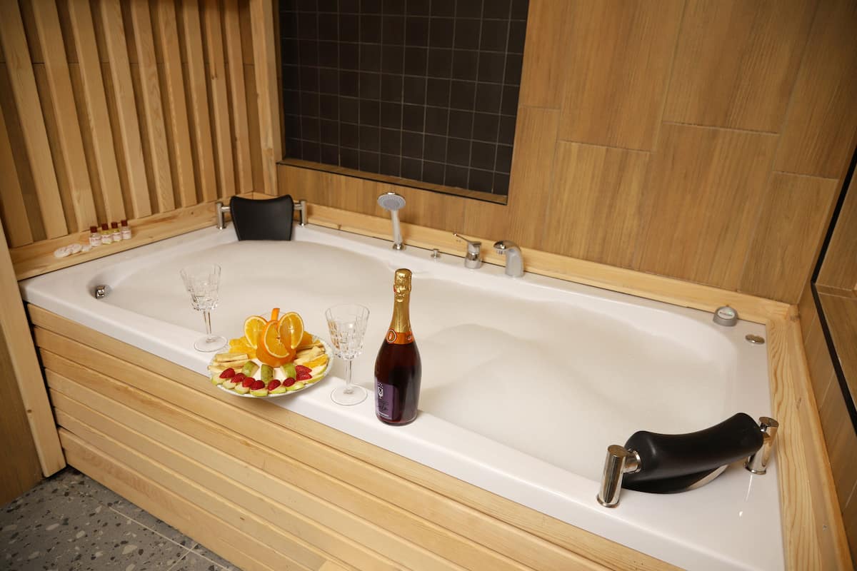 A bathtub with a bottle of champagne, a glass, and a fruit bowl.