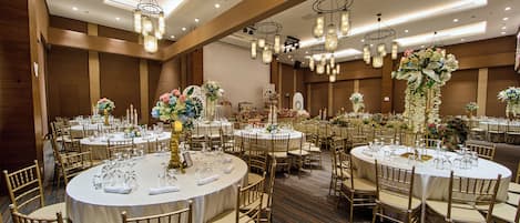 A banquet hall with round tables, gold chairs, and floral centerpieces.