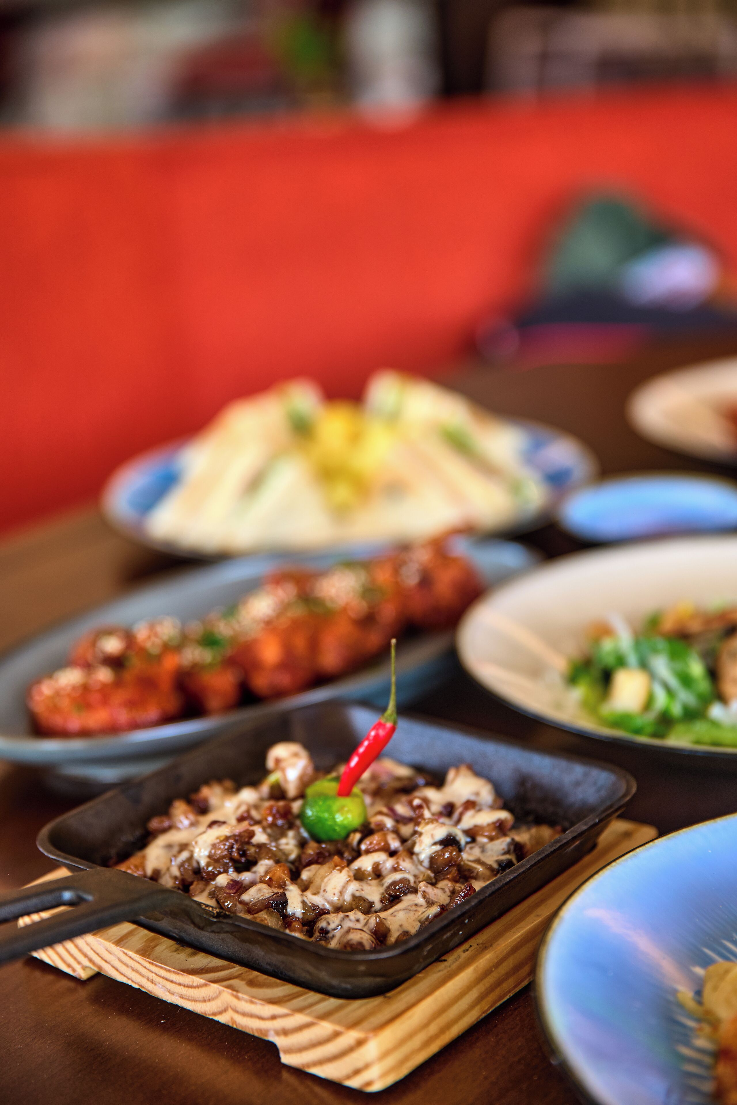 A variety of dishes on a table, including a skillet with food and a red chili.