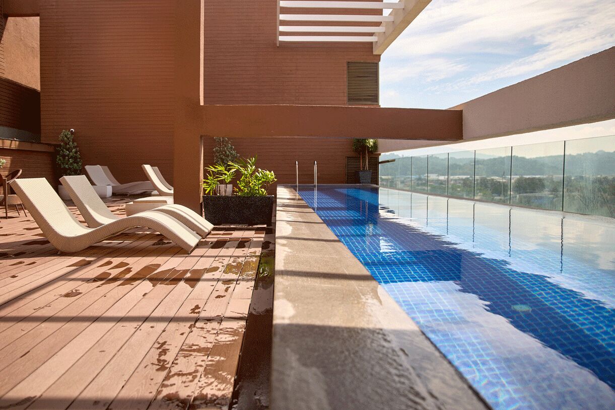 An outdoor infinity pool with lounge chairs, a wooden deck, and a view of the city skyline.