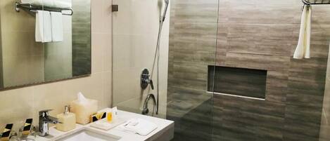 A modern bathroom with a large mirror, a sink with toiletries, a shower, and a towel rack.