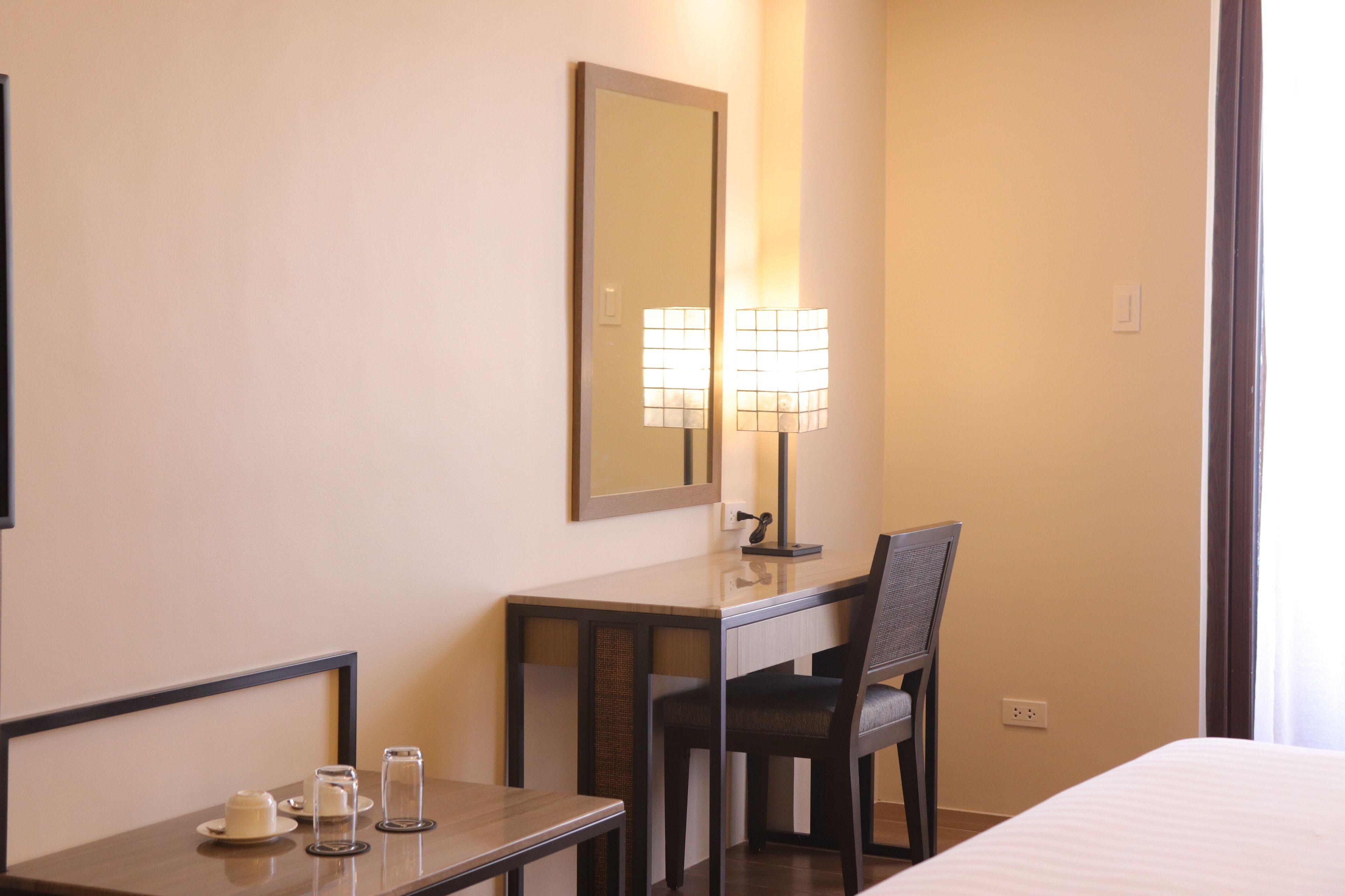 Une chambre d’hôtel avec un lit, un bureau avec une chaise, une lampe et un miroir.