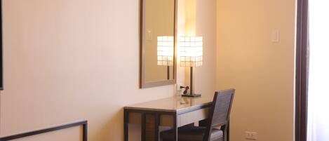 Una habitación de hotel con cama, escritorio, silla, lámpara y espejo.