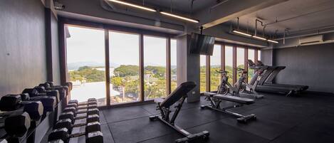 A gym with exercise equipment, large windows, and a view of a cityscape.