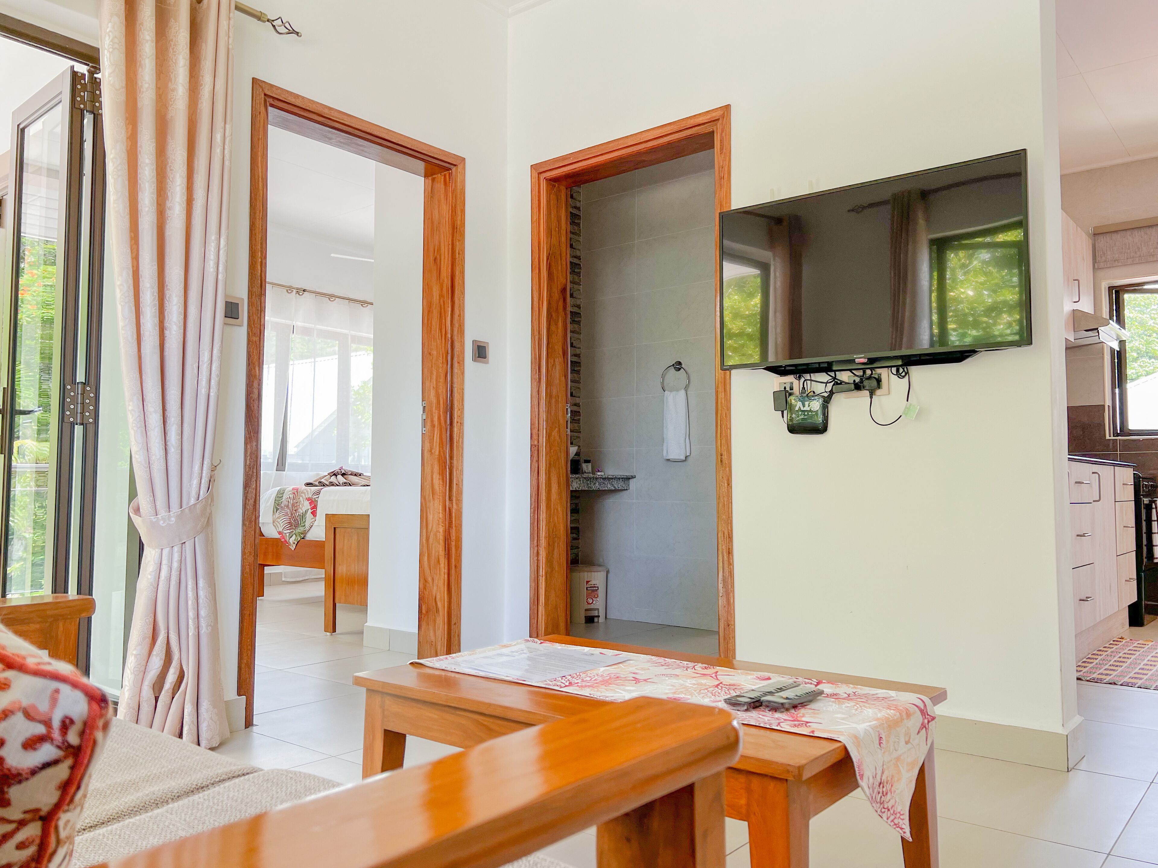 A room with a wooden table, a sofa, and a view of a kitchen and bathroom through an open door.