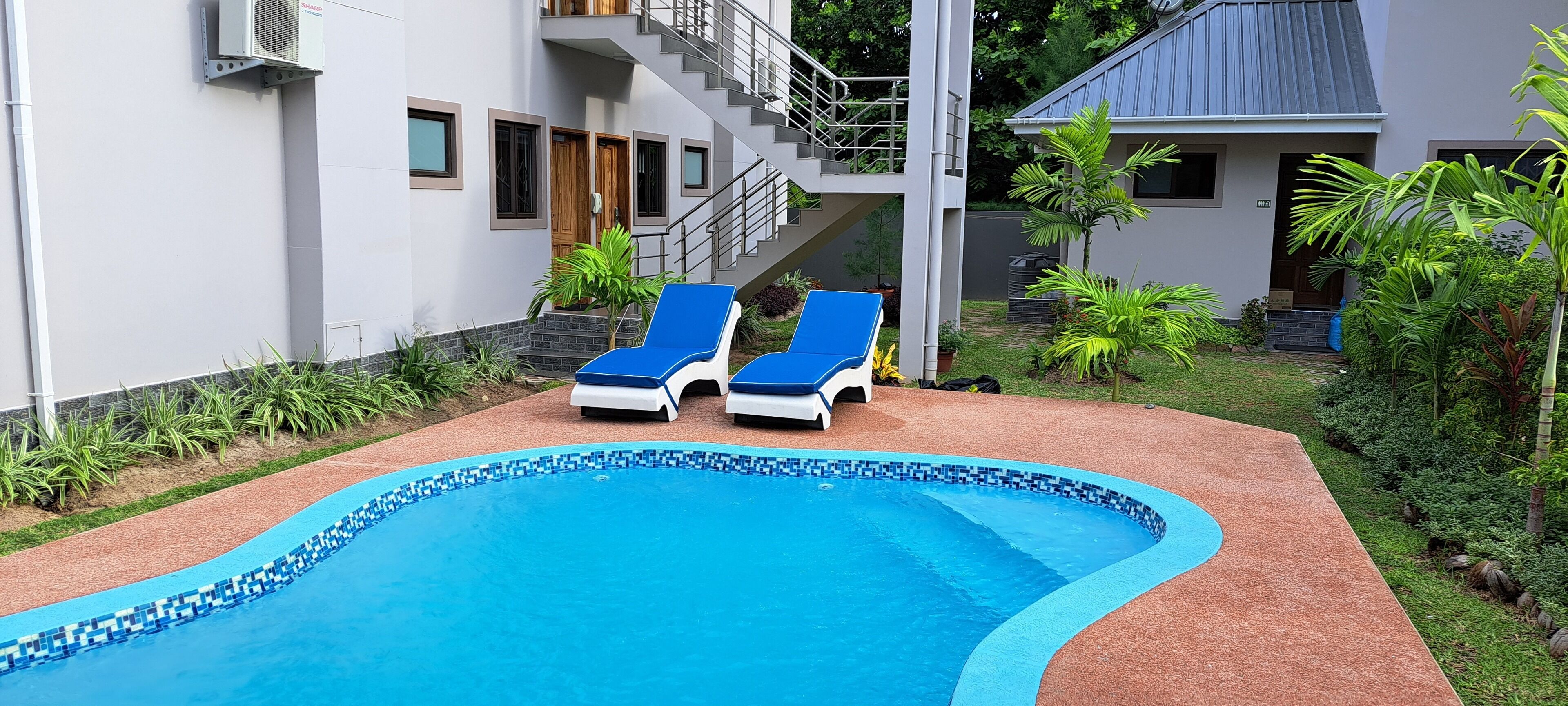 A swimming pool with two lounge chairs, surrounded by a garden with various plants and a staircase leading to a building.