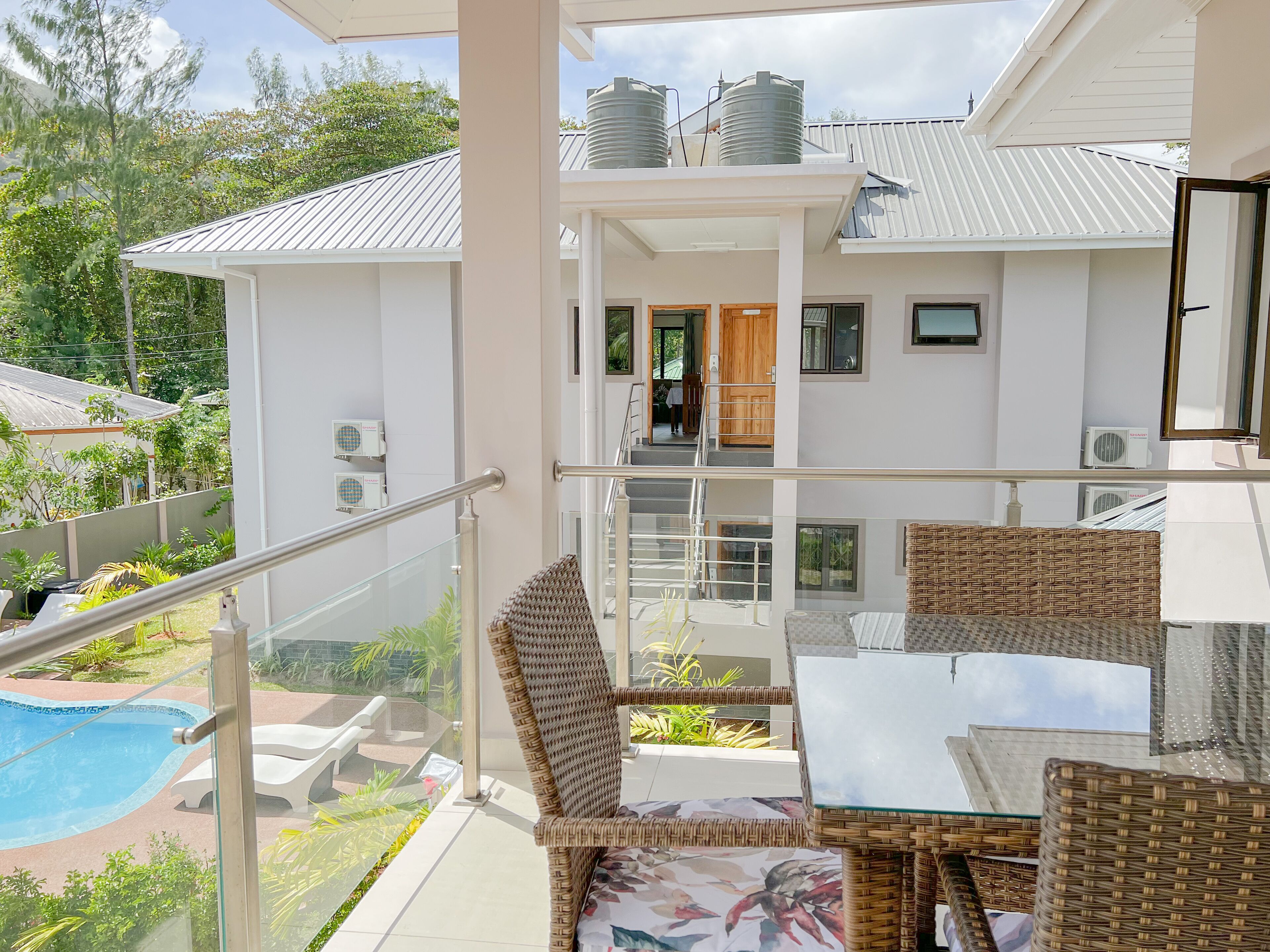 A balcony with wicker furniture, a glass table, and a pool.