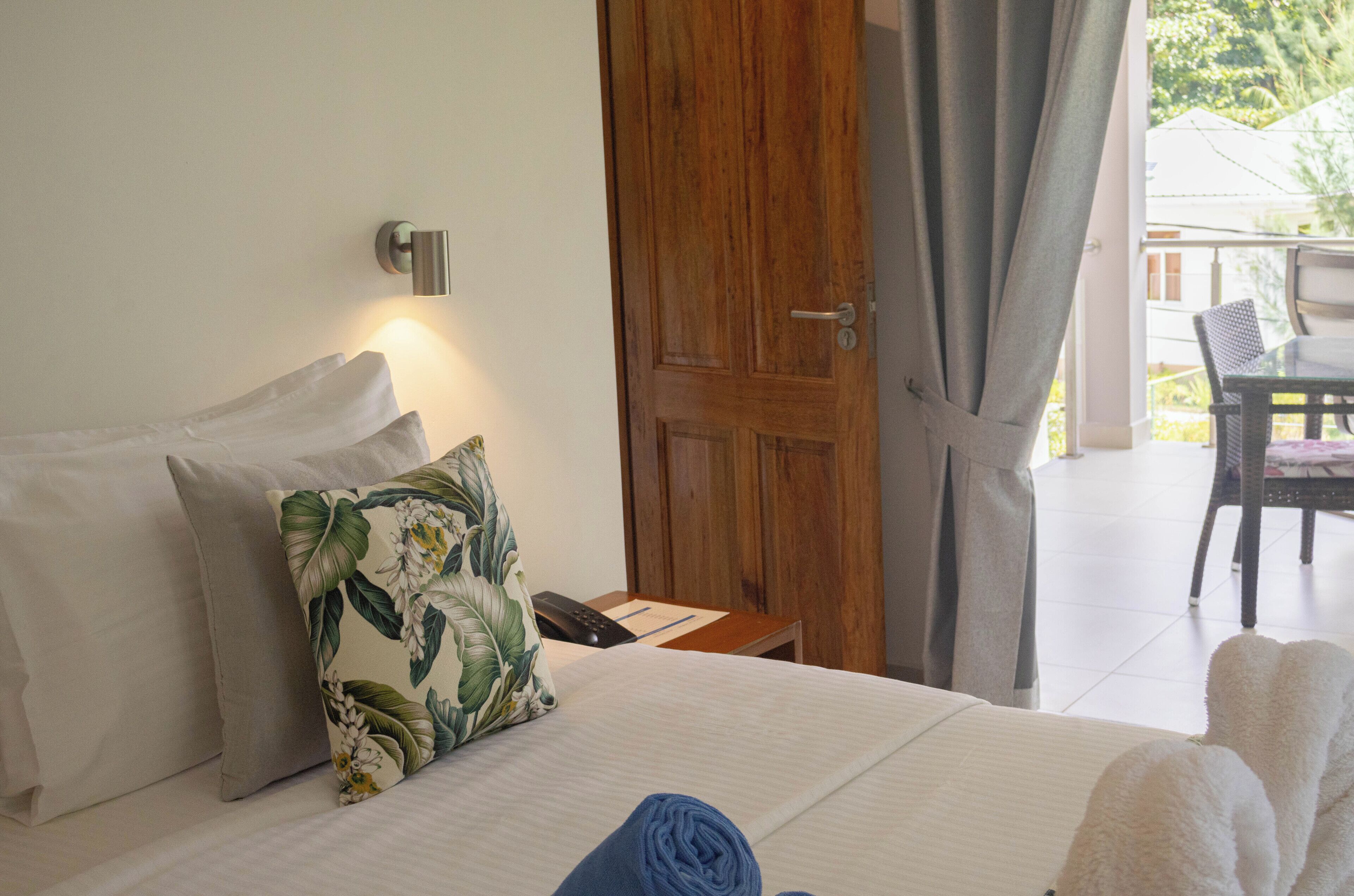 A hotel room with a bed, a wooden door, a telephone, and a view of the outside.