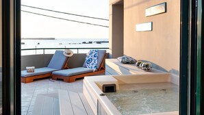 Een balkon met twee lounge fauteuils, een jacuzzi en uitzicht op zee.