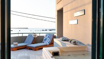 A balcony with two lounge chairs, a hot tub, and a view of the sea.