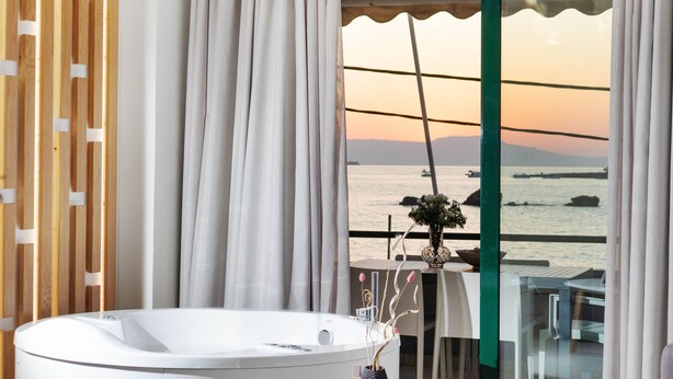 Een badkamer met een bad, uitzicht op zee en een tafel met een vaas en bloemen.