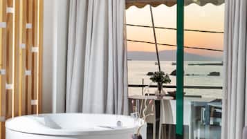 Een badkamer met een bad, uitzicht op zee en een tafel met een vaas en bloemen.
