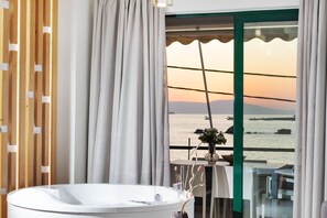 A bathroom with a bathtub, a view of the sea, and a table with a vase and flowers.