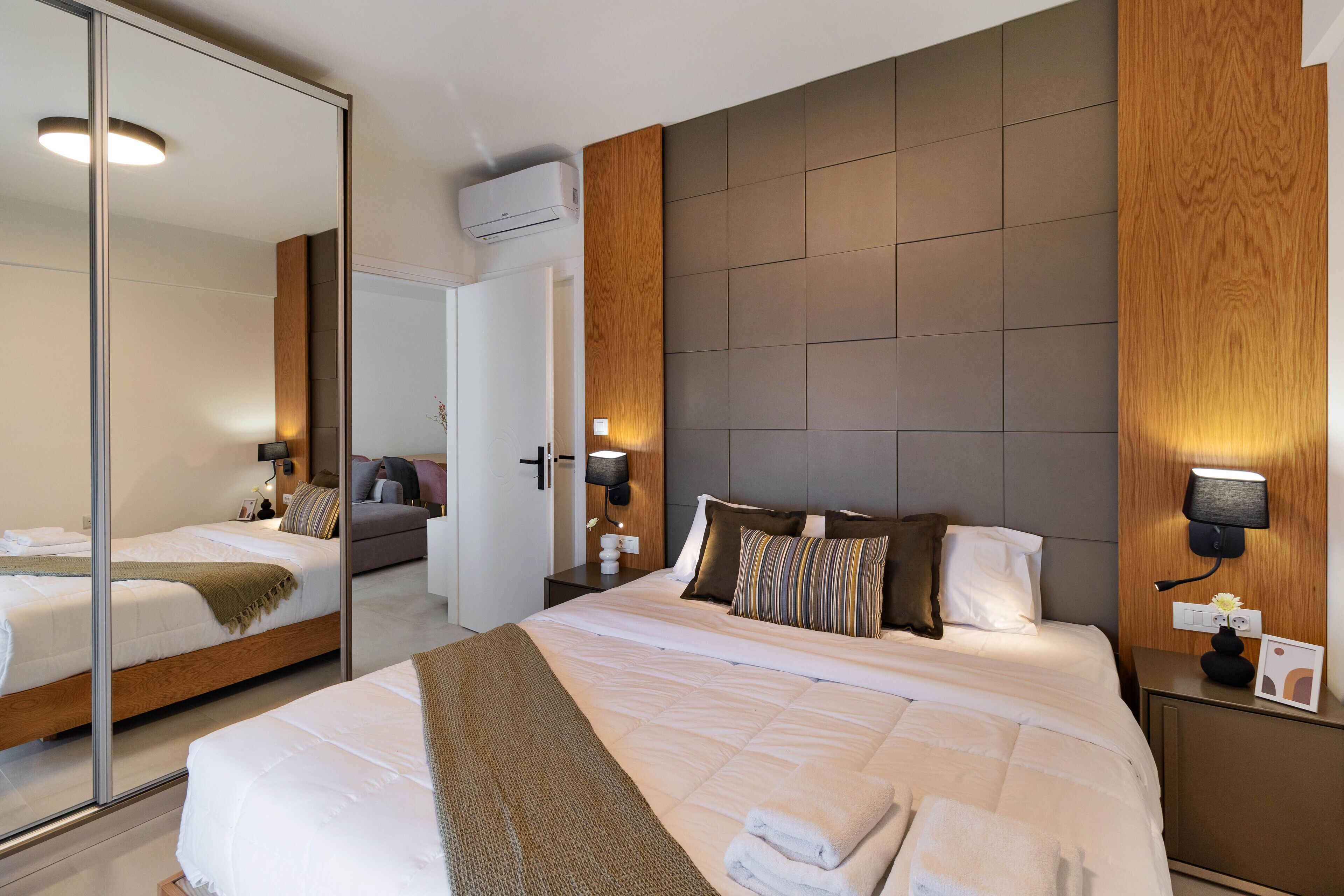 Een hotelkamer met een groot bed, een spiegel, een houten hoofdbord en een nachtkastje met een lamp.