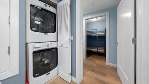 A laundry room with two washing machines, a dryer, and a bunk bed in the adjacent room. - La Jolla Ocean Front Escape (San Diego)