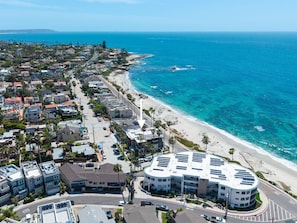 An aerial view of a coastal residential area with a beachfront, a parking lot, and a multi-story building with a curved facade. - La Jolla Ocean Front Escape (San Diego)
