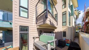 A balcony with a wooden chair and a small table, a window, and a building with multiple floors and balconies. - La Jolla Ocean Front Escape (San Diego)