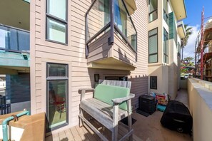 A balcony with a wooden chair and a small table, a window, and a building with multiple floors and balconies. - La Jolla Ocean Front Escape (San Diego)