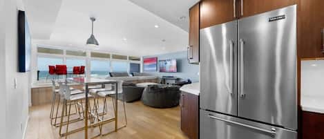 A modern kitchen with a stainless steel refrigerator, wooden cabinets, and a dining area with bar stools.