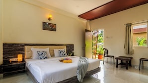 A bedroom with a large bed, bedside tables, a nightstand, a window with curtains, and a view of greenery outside. - Arnnas Resort Diveagar (Shrivardhan)
