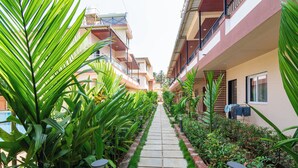 A pathway flanked by lush greenery and modern buildings with balconies. - Arnnas Resort Diveagar (Shrivardhan)