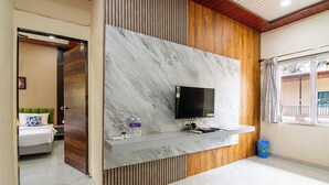 A modern hotel room with a marble wall, a mounted TV, and a wooden accent wall. - Arnnas Resort Diveagar (Shrivardhan)