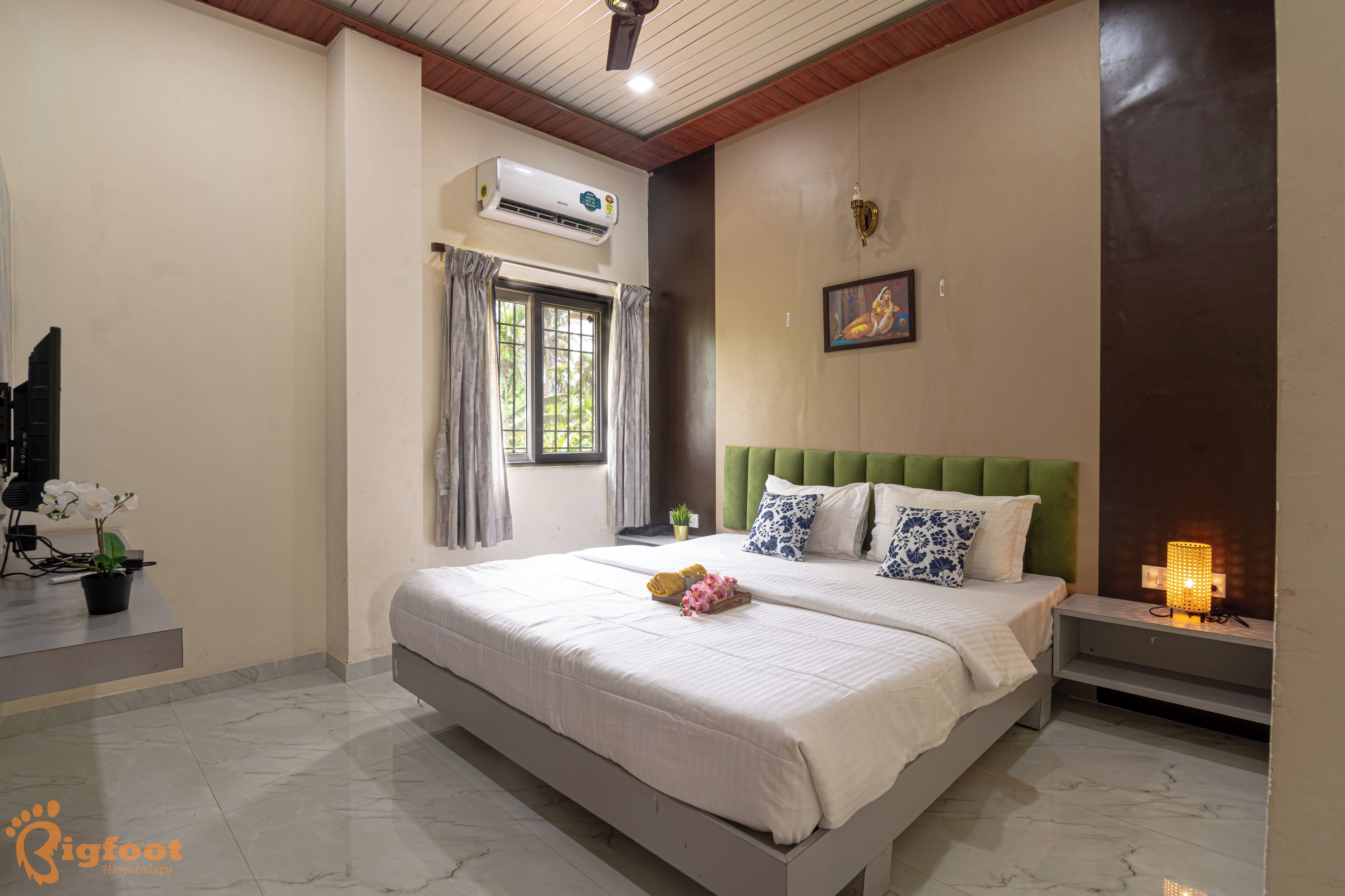 A bedroom with a large bed, a nightstand, an air conditioning unit, and a window with curtains.