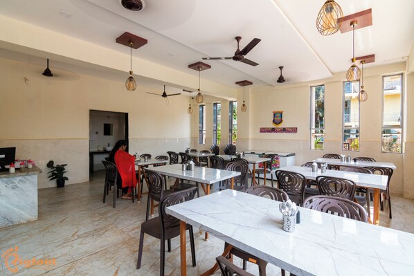A spacious dining area with marble tables and chairs, ceiling fans, and pendant lighting.