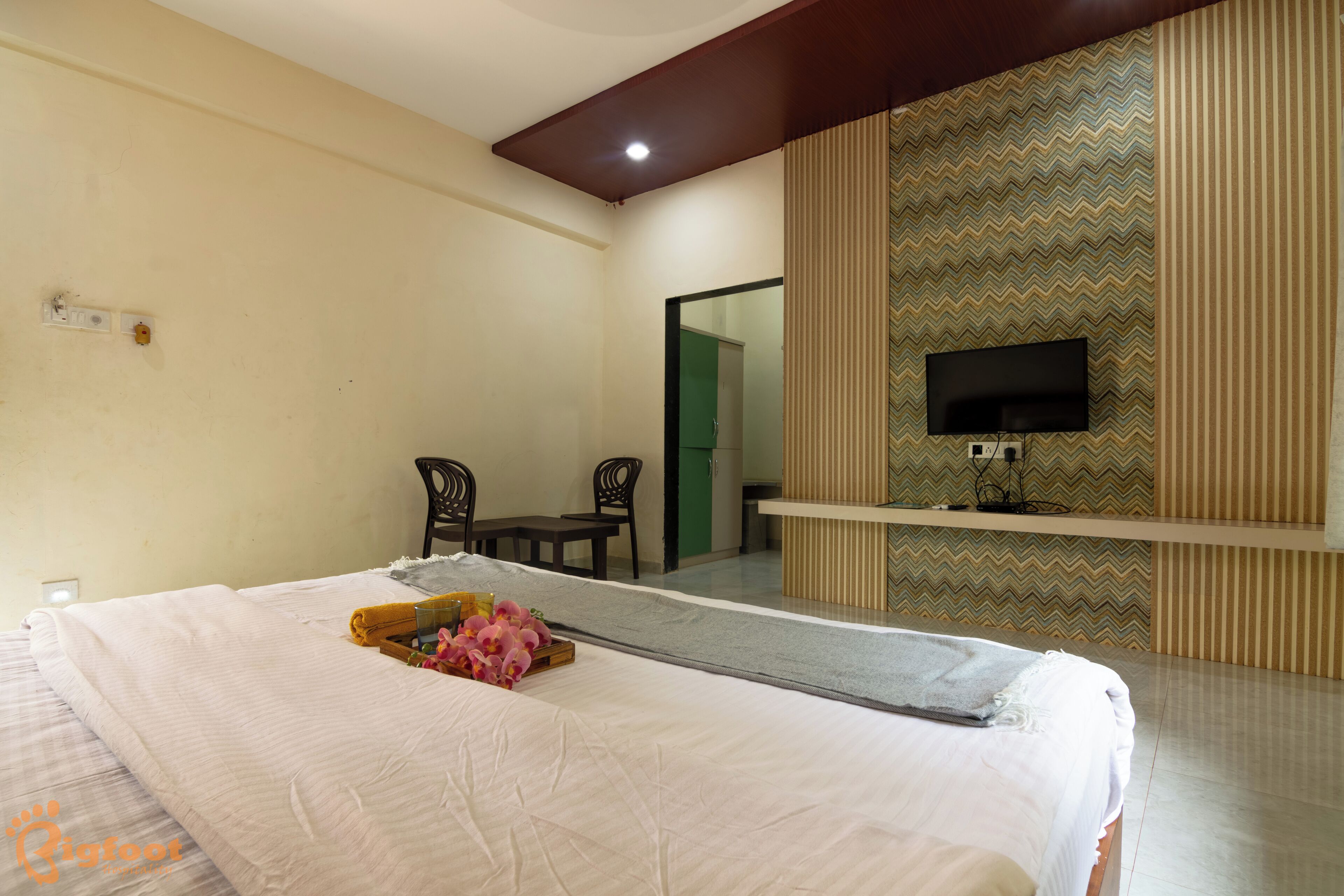 A hotel room with a bed, a TV mounted on the wall, a desk, and chairs.