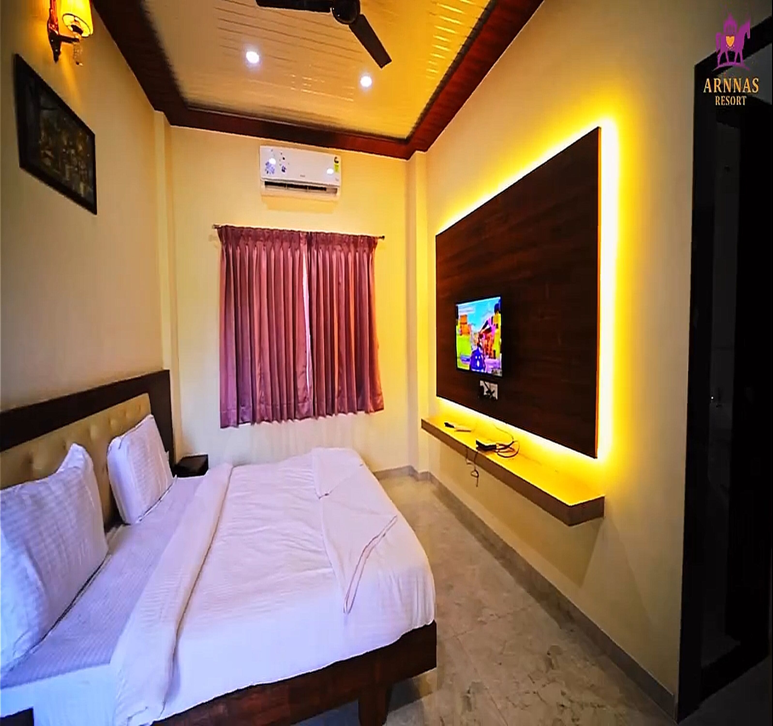 A hotel room with a bed, a TV mounted on the wall, and a ceiling fan.