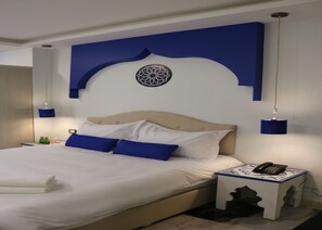 A neatly made bed with white linens and blue pillows, a bedside table with a phone, and a decorative wall piece above the bed. - Amman Trail Hotel & Studios (Amman)