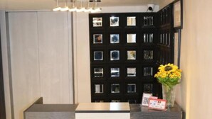 A reception desk with a modern design, featuring a dark wood finish and a white panel. There is a vase with yellow flowers on the right side of the desk. - Amman Trail Hotel & Studios (Amman)