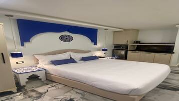 Quarto de hotel com uma cama grande, mesa de cabeceira, escrivaninha, micro-ondas e geladeira.
