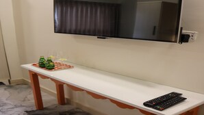 A flat-screen TV mounted on a wall above a white console table with a remote control on it. - Amman Trail Hotel & Studios (Amman)