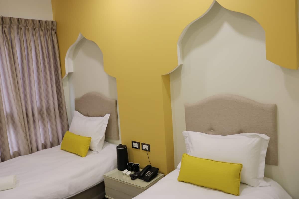 A hotel room with two beds, each with a headboard, a nightstand with a phone and a lamp, and a curtain.