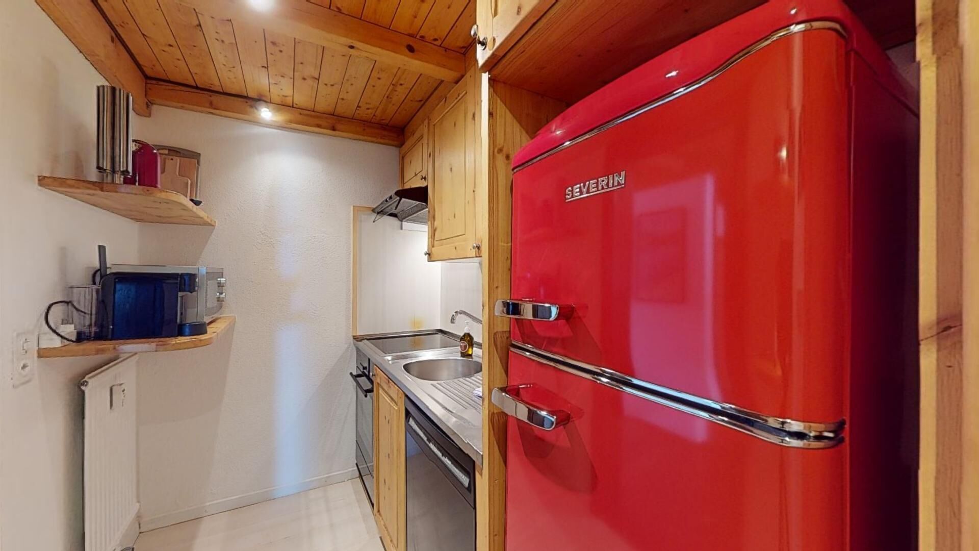 A compact kitchen with a red refrigerator, wooden cabinets, and a small countertop with a coffee machine.