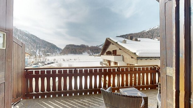 Un balcon en bois offrant une vue sur un paysage enneigé et sur un bâtiment doté d’un toit en pente.