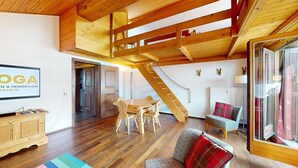 Une pièce spacieuse avec un plafond en bois, un coin repas comprenant une table et des chaises, un canapé et un escalier menant à un niveau supérieur.