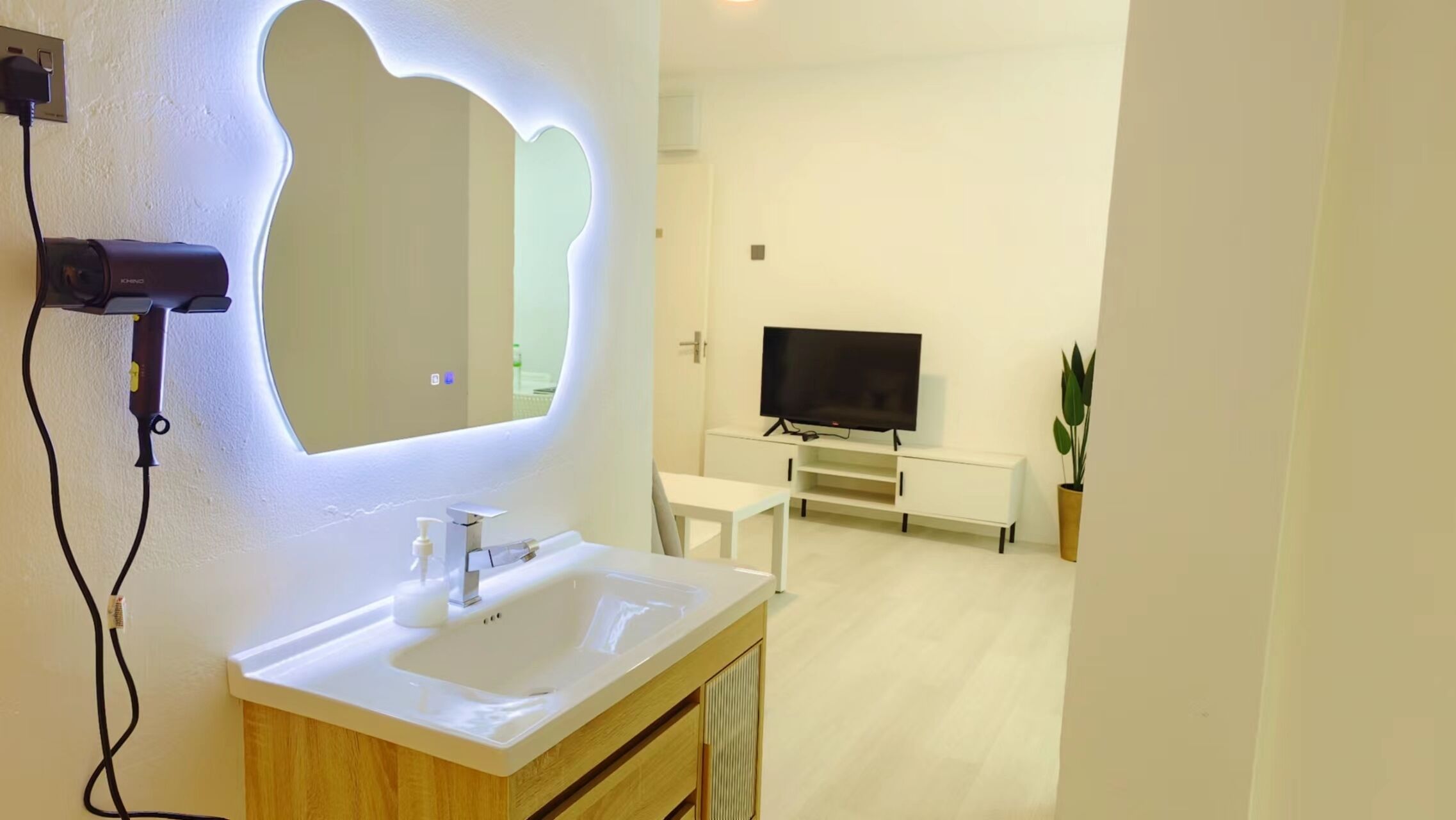 A modern bathroom with a vanity, sink, and mirror. There is a TV in the adjacent living area.